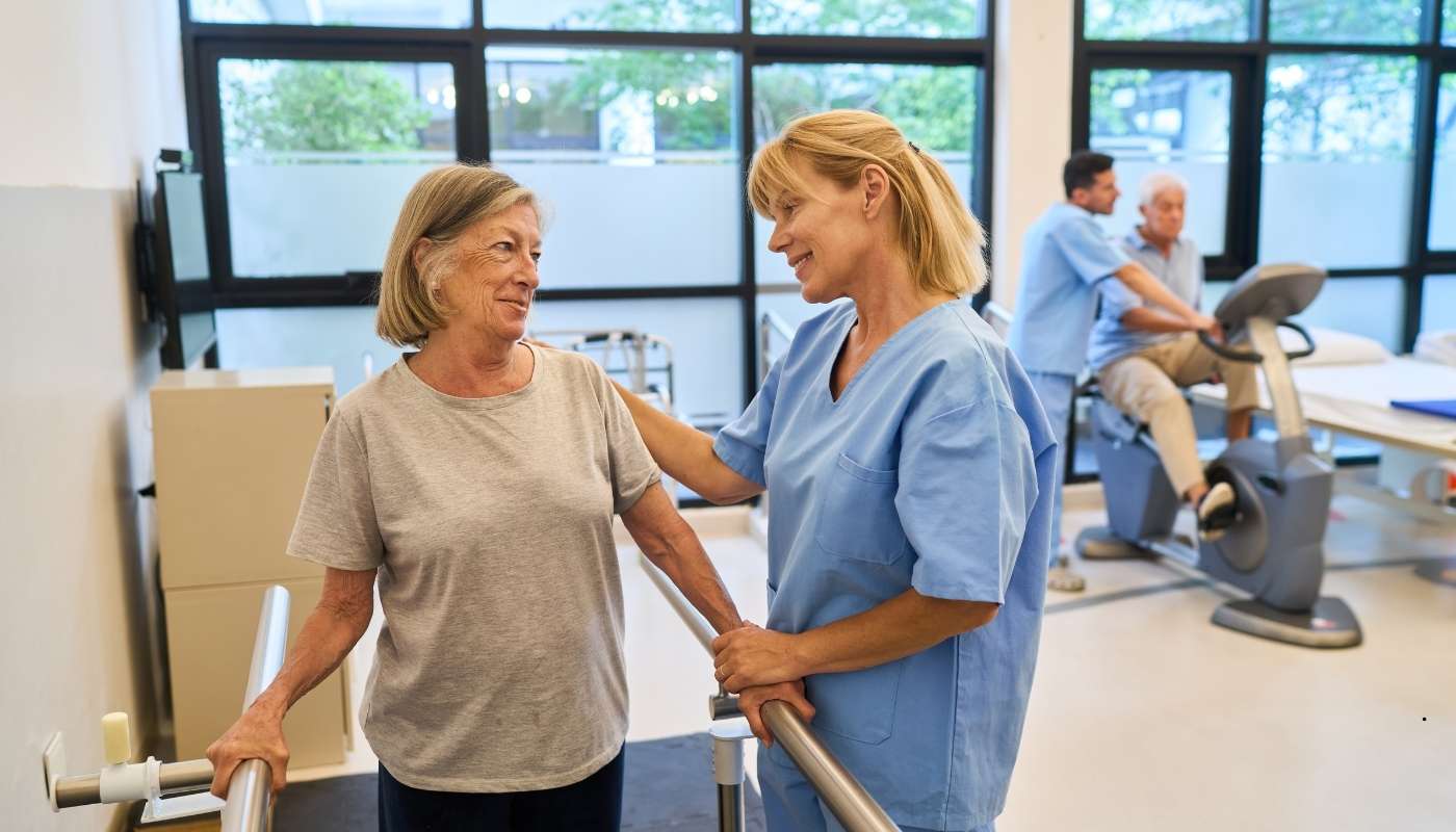 أخصائي علاج طبيعي يساعد مسنًا محدود الحركة في تمرين تقوية، ضمن برنامج التأهيل الحركي الشامل.