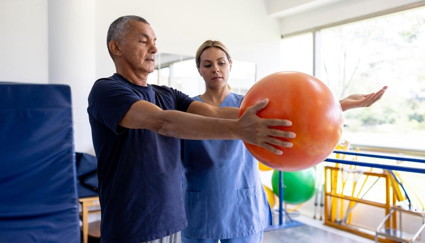 علاج طبيعي بعد العمليات لكبار السن أخصائي يساعد مسنًا بعد جراحة استبدال مفصل على المشي بأمان، ضمن جلسات العلاج الطبيعي والتأهيل الحركي